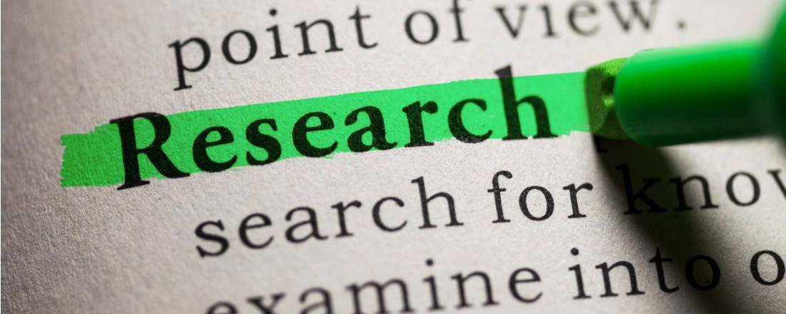 Paper with printed text, the word "Research" is being highlighted with a green text marker